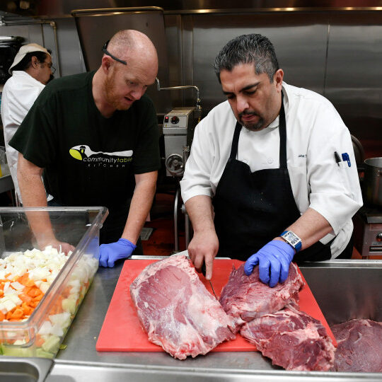 BOULDER, CO - DECEMBER:  Chef John Trejo, right, teaches James, who did not want his last name used, how to cut a large portion of meat at the Community Table Kitchen on December 19, 2017 in Boulder, Colorado. Trejo helps over see the kitchen for people who belong to Bridgehouse. Bridgehouse is a "community to work" program for people who are homeless.  People are trained in jobs skills that will help them when they look for work.  and others, who were homeless last year, have transitioned to living in a home.  They have been trained in culinary school and are helping to prepare a Christmas day meal for the homeless in the area. (Photo by Helen H. Richardson/The Denver Post)